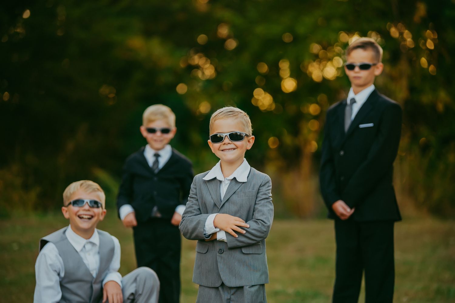 Groomsmen wearing matching gray suits and sunglasses pose outdoors in autumn.
