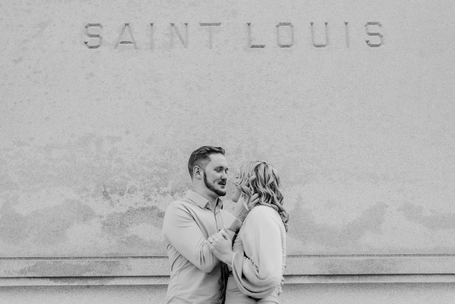 Black and white photo of a couple sharing a romantic moment in front of a Saint Louis wall.
