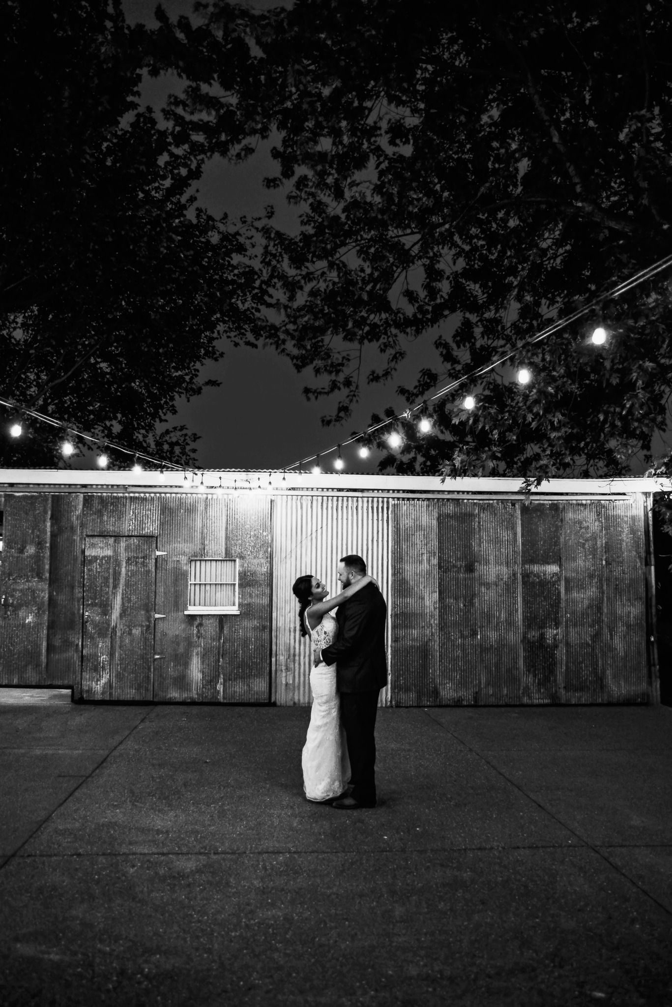 Black and white nighttime wedding reception with string lights and rustic wooden backdrop.