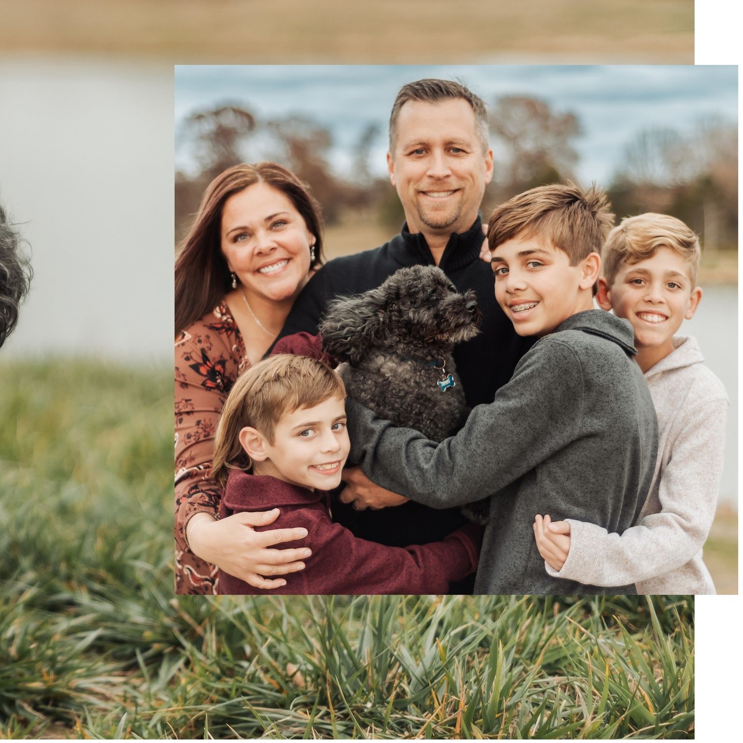 Family members embrace while sitting in tall grass during golden hour.