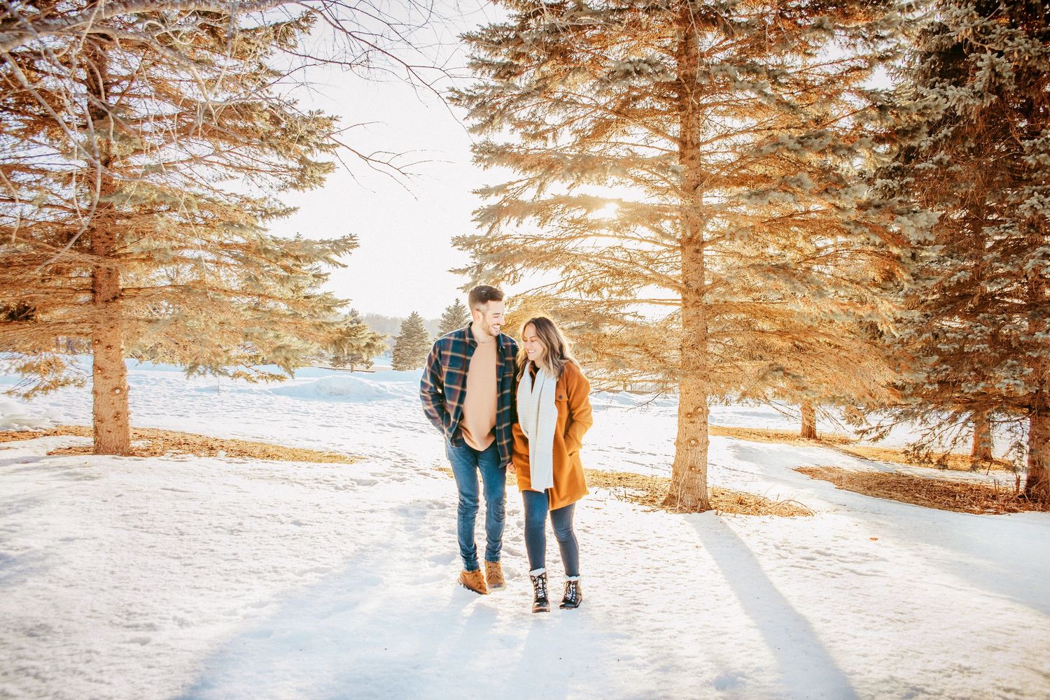 Couple walking together on snowy path through sunlit winter pine forest.