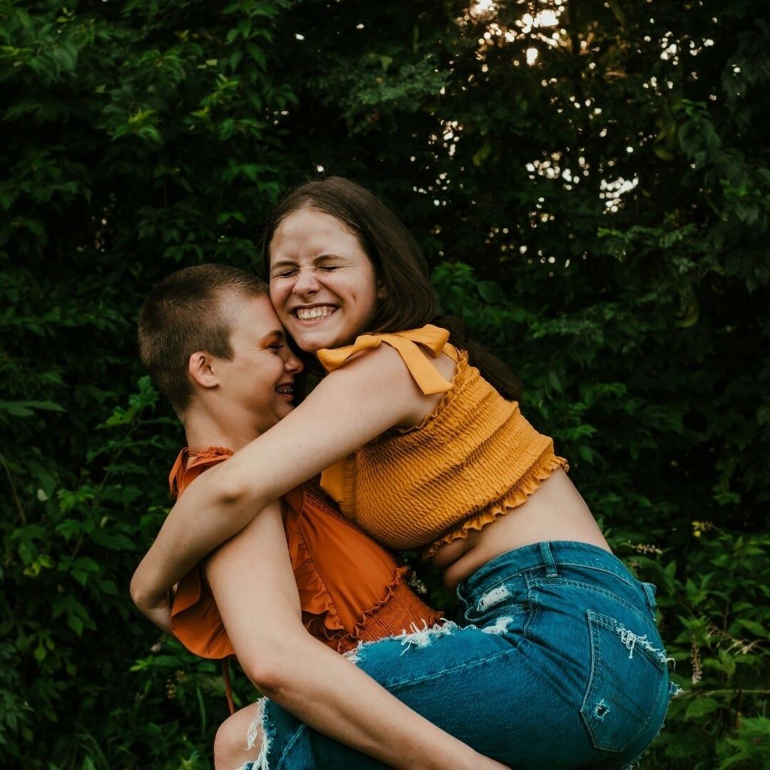 Playful outdoor embrace with mustard yellow and denim outfits in forest setting.