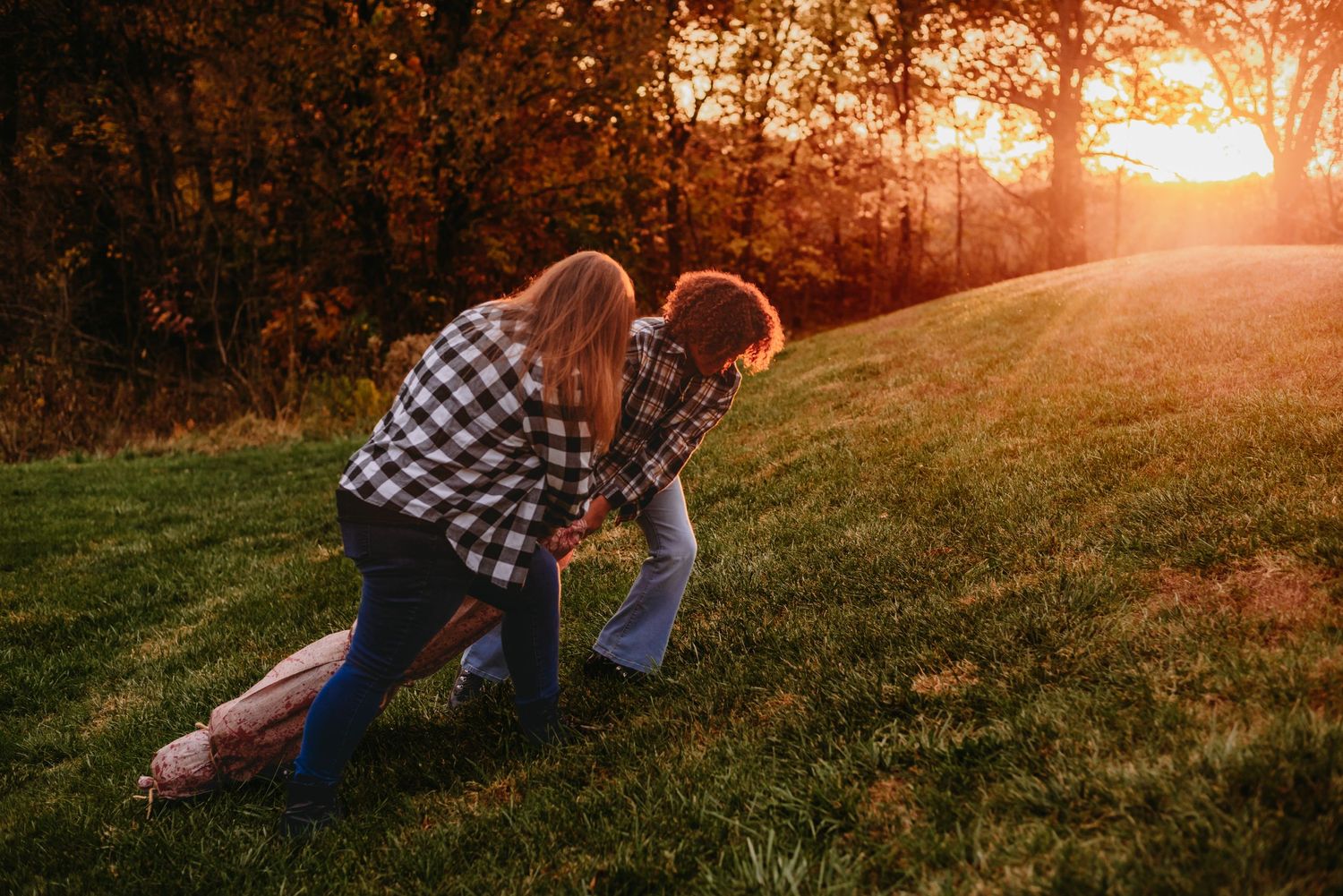 Couple playfully embracing on grassy hill during golden sunset.