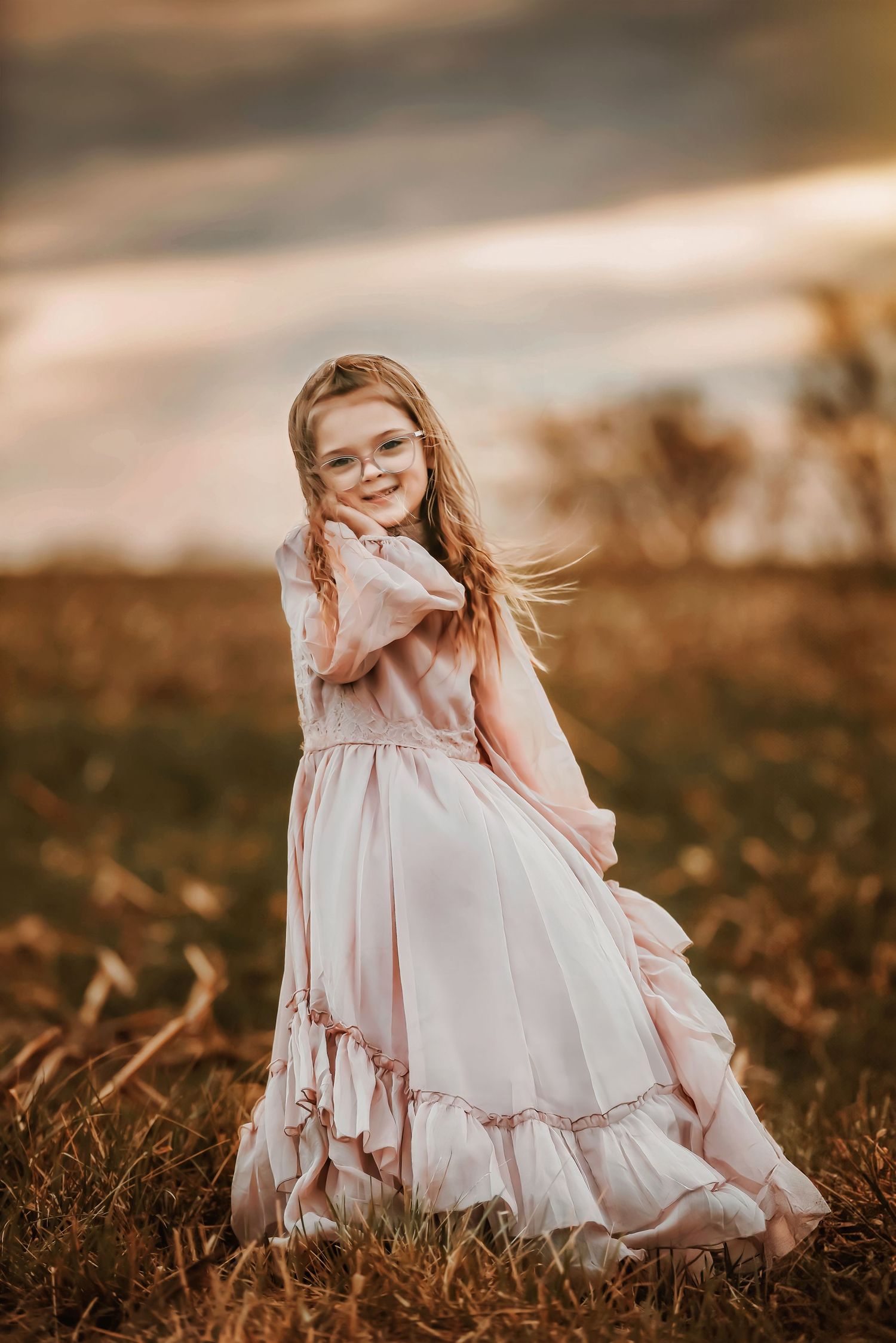 Young girl in flowing pink dress twirling outdoors at sunset.
