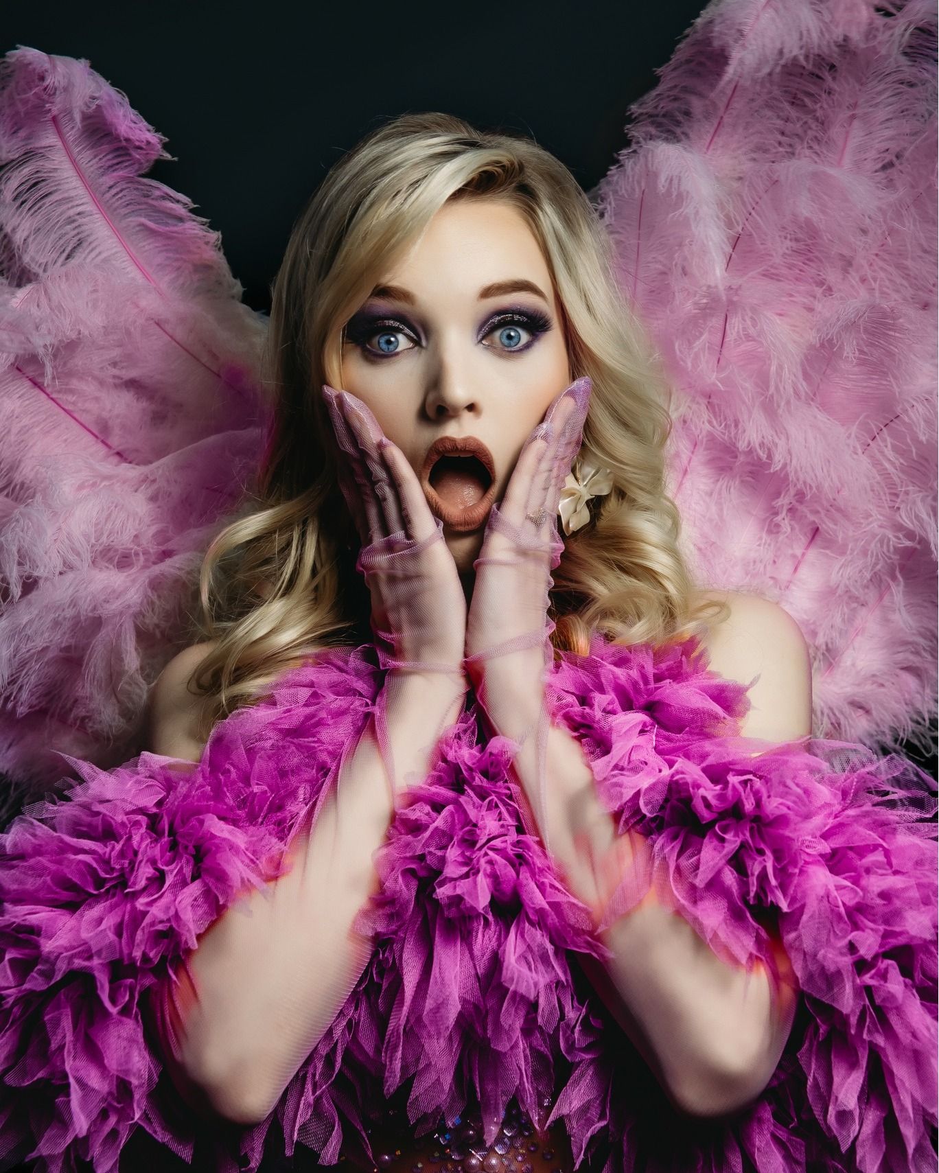 Dramatic portrait with pink feathered wings and matching feather boa against dark background.