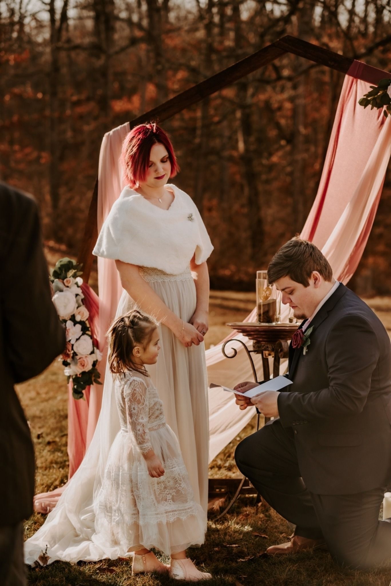 Outdoor wedding ceremony setup with pink drapes and floral decorations in autumn woods.