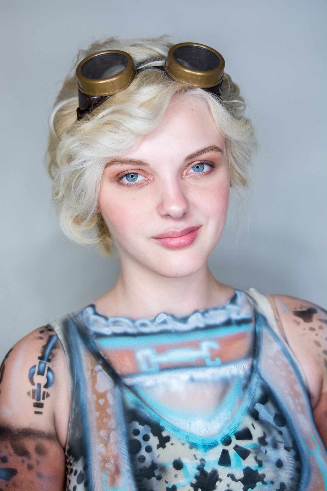 Portrait with steampunk goggles and artistic outfit against gray background.