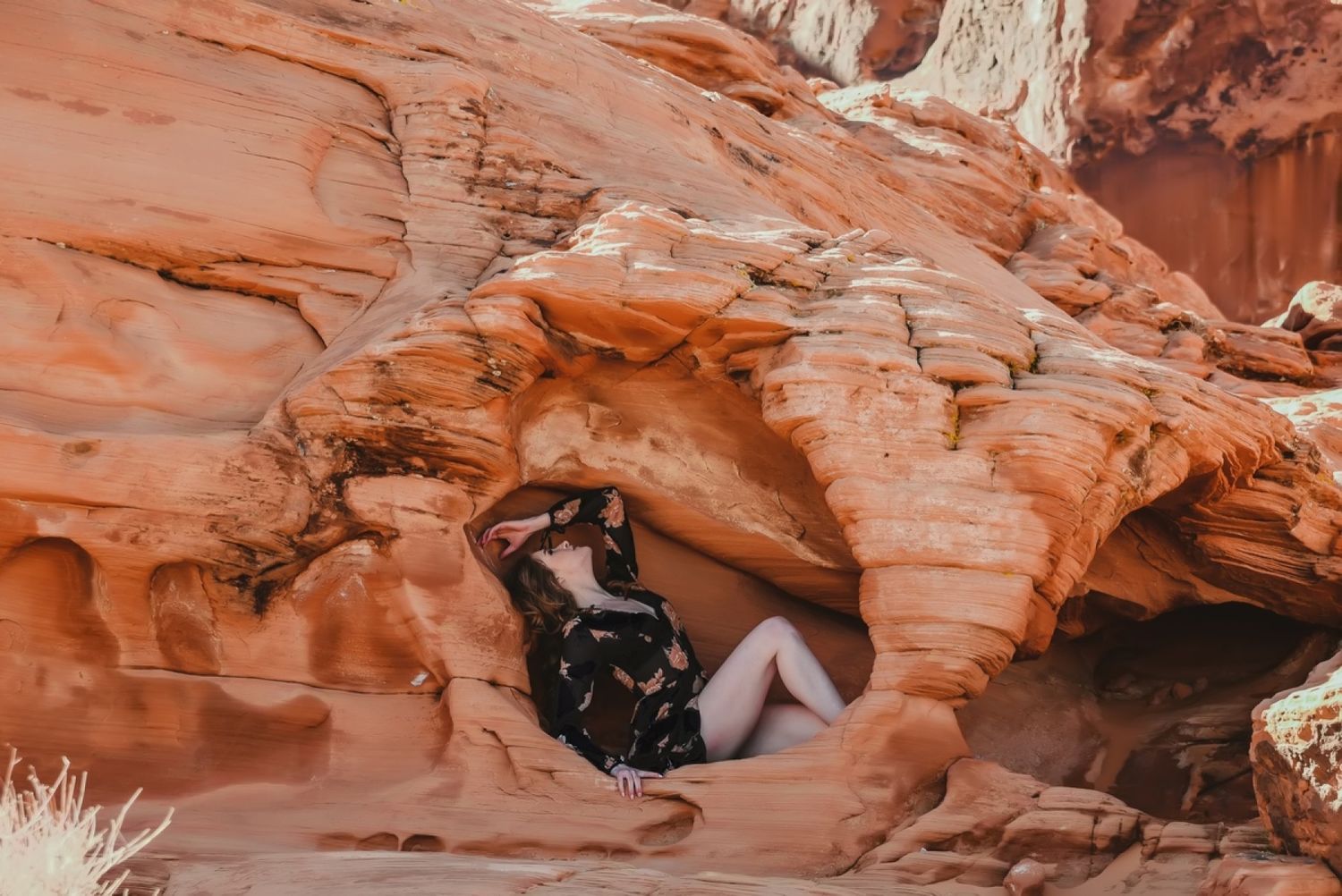 Person resting in a natural red rock cave formation in the desert landscape.