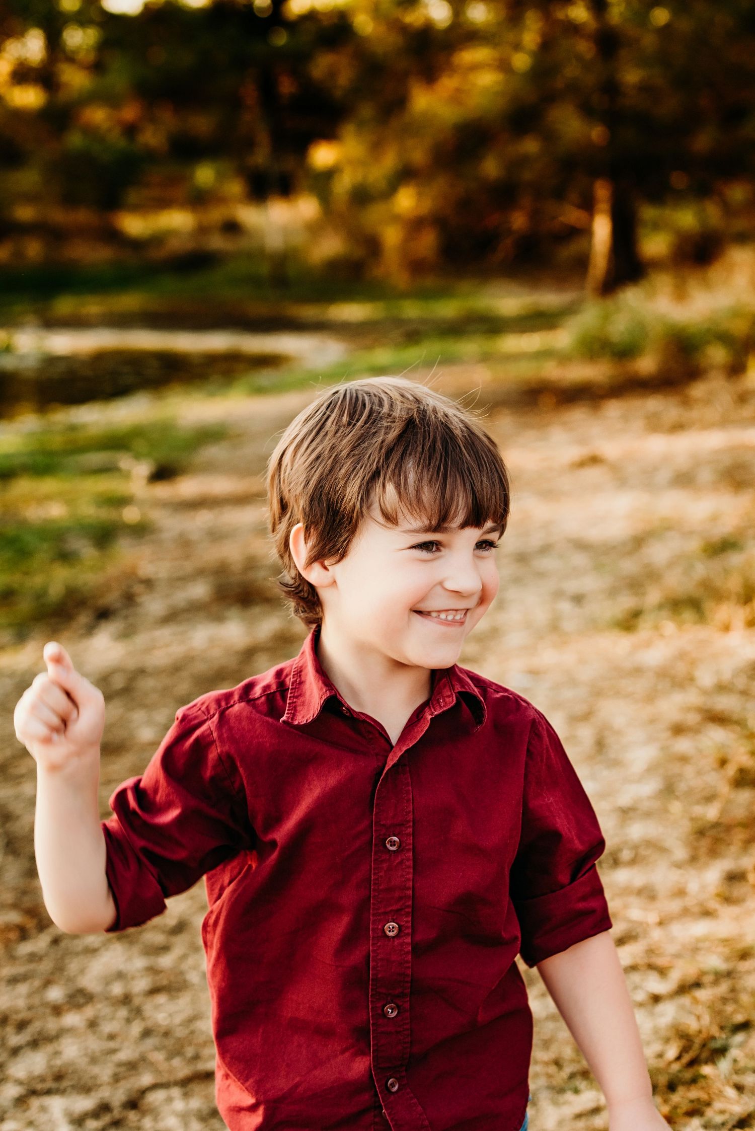 A person in a burgundy button-up shirt smiles and dances joyfully in an autumn outdoor setting.