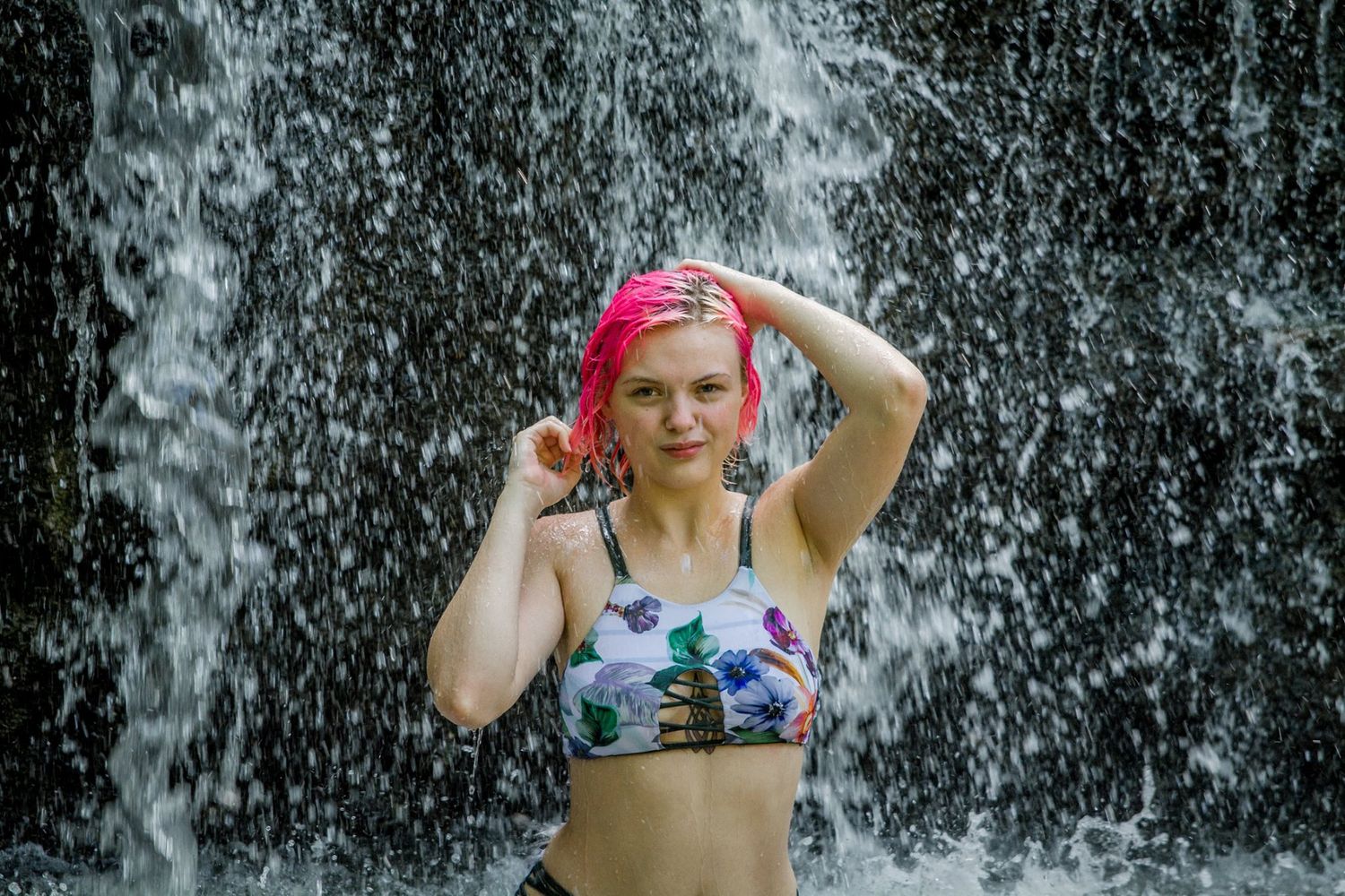 Person in swimwear poses under cascading waterfall spray.