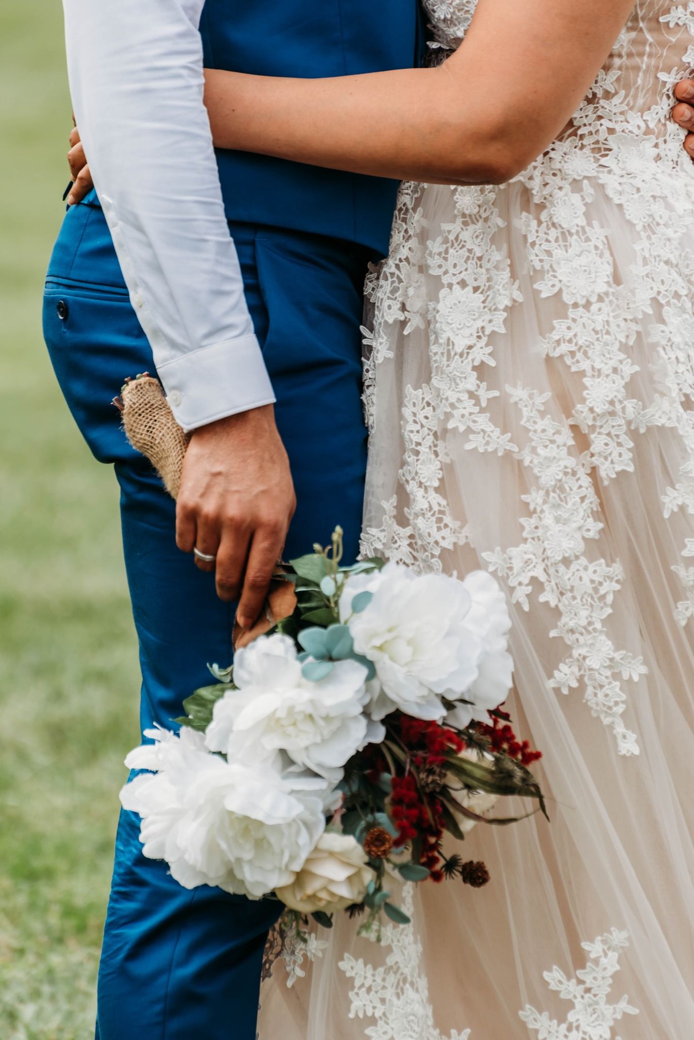 Wedding detail shot of lace dress and white floral bouquet with navy suit.