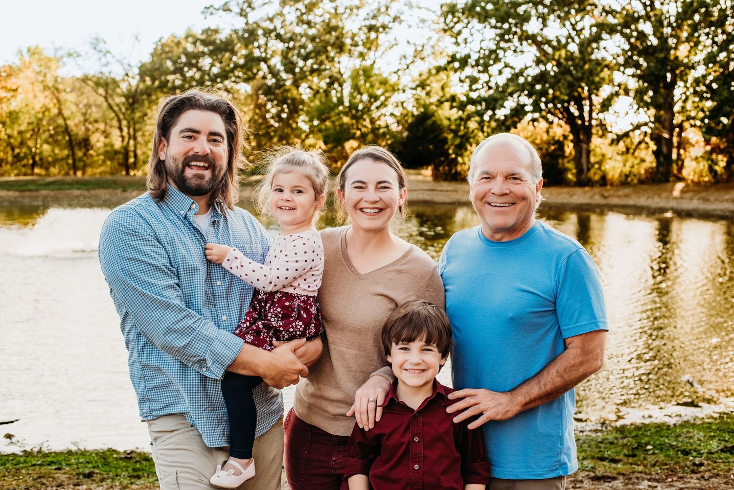 Multi-generational family smiling together by lake during autumn sunset.