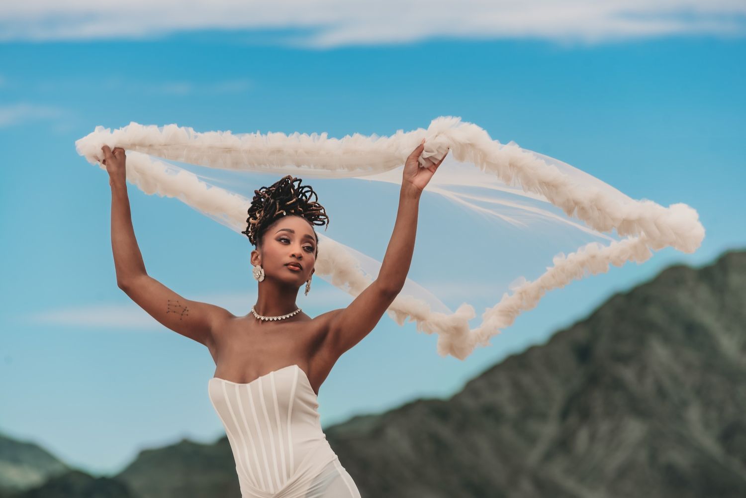 Joyful bride celebrating against mountain backdrop with veil flowing in the wind.