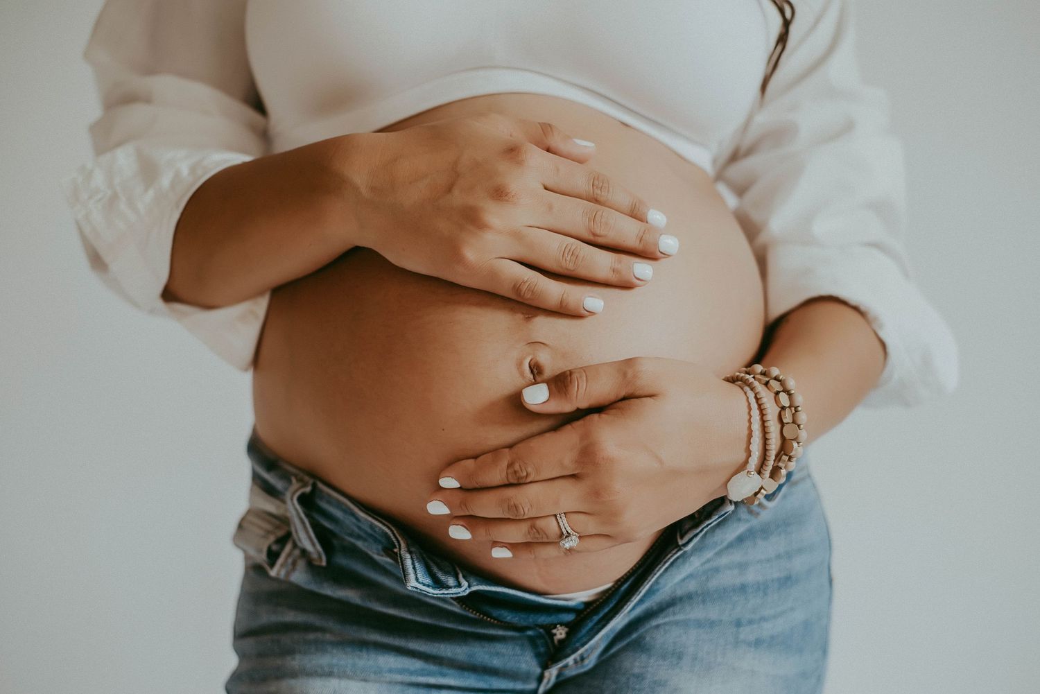 Close-up of pregnant belly with hands gently cradling the bump, wearing casual denim.