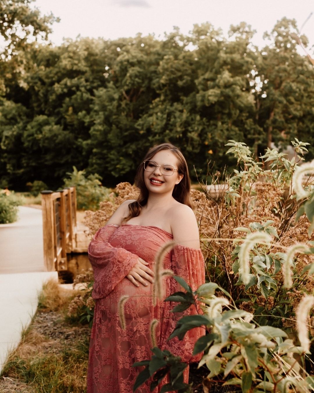Maternity photos in a garden setting with woman wearing flowing pink lace dress.