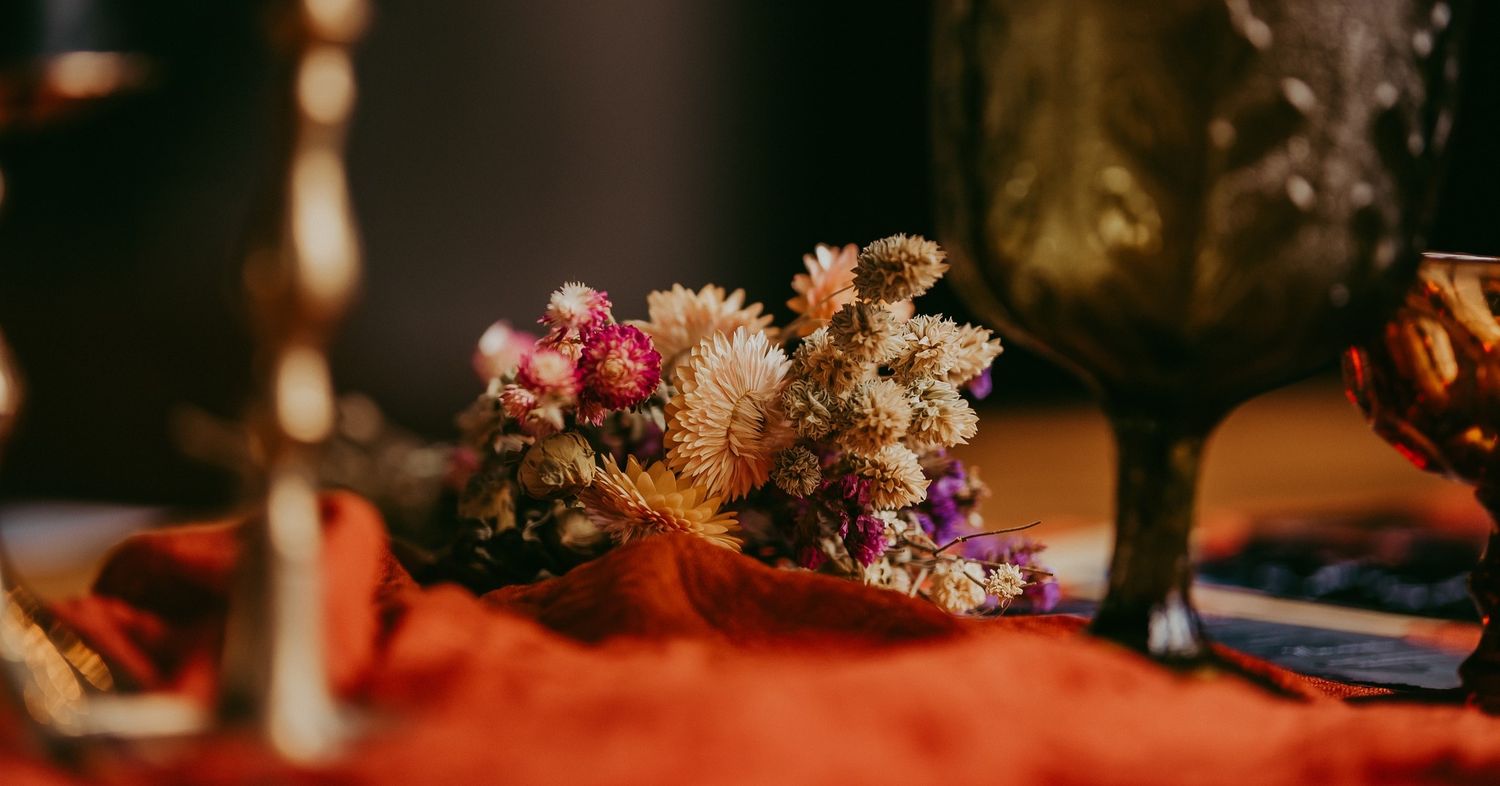 Dried flowers and berries arranged on an orange tablecloth in moody lighting.