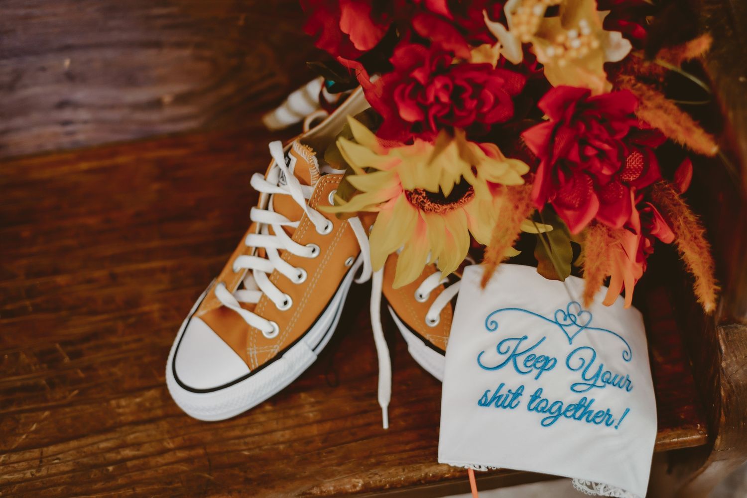 Yellow Converse sneaker with red flowers and wedding details on wooden surface.