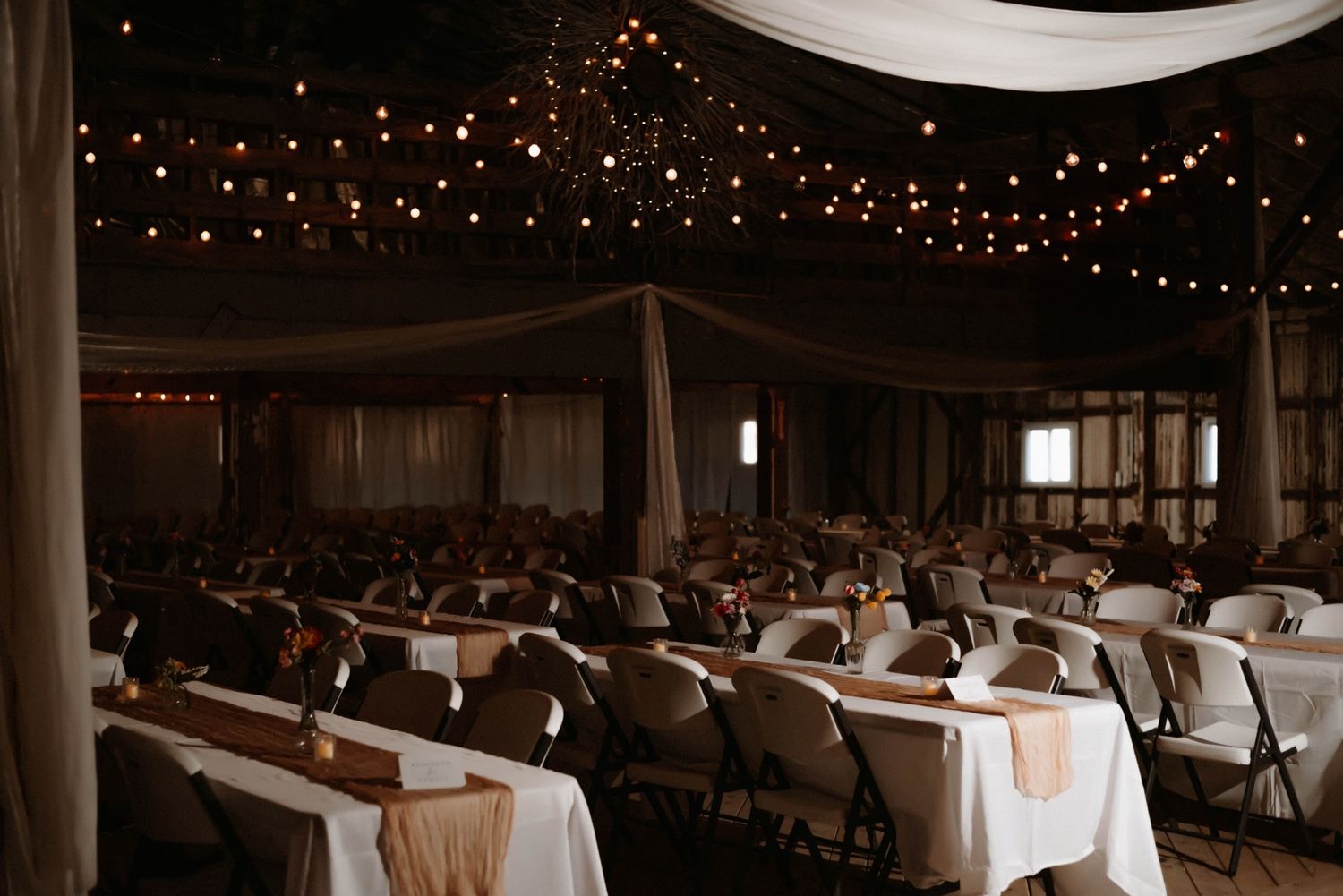 Wedding reception venue decorated with romantic string lights and white table settings.