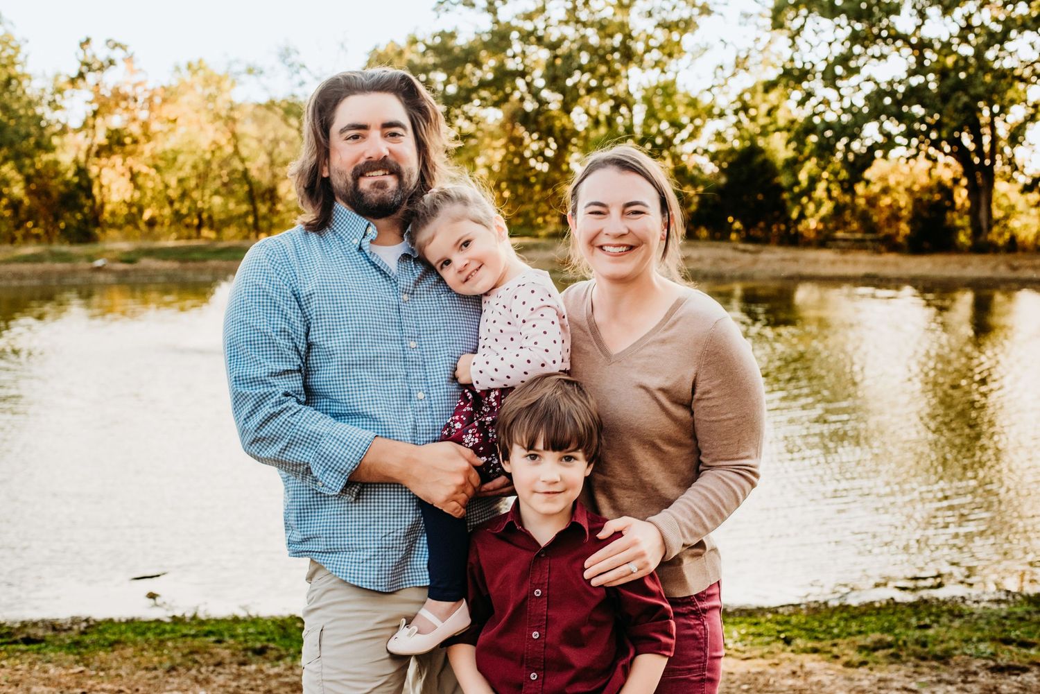 A happy family poses together outdoors near a lake during golden hour in autumn.