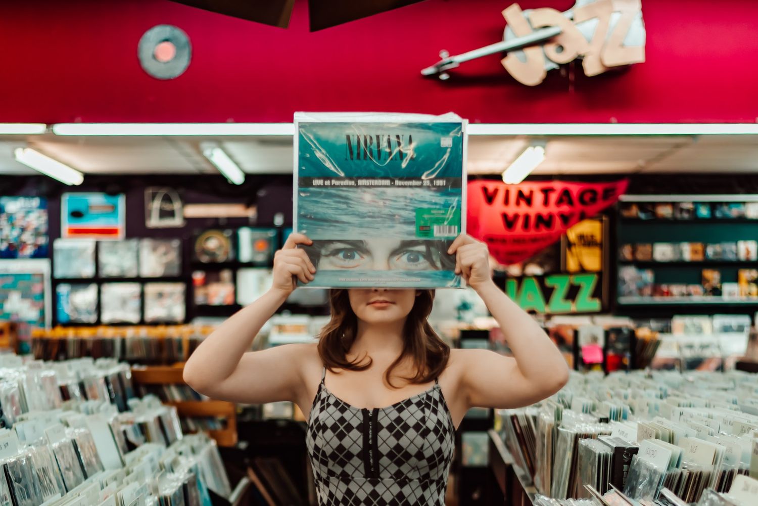 Person holding up a vintage vinyl record in front of their face while browsing in a record store.