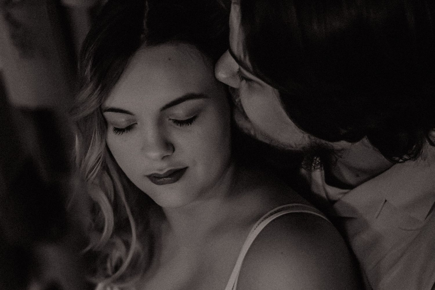 A romantic black and white photo of a couple in an intimate embrace with soft lighting and dramatic shadows.