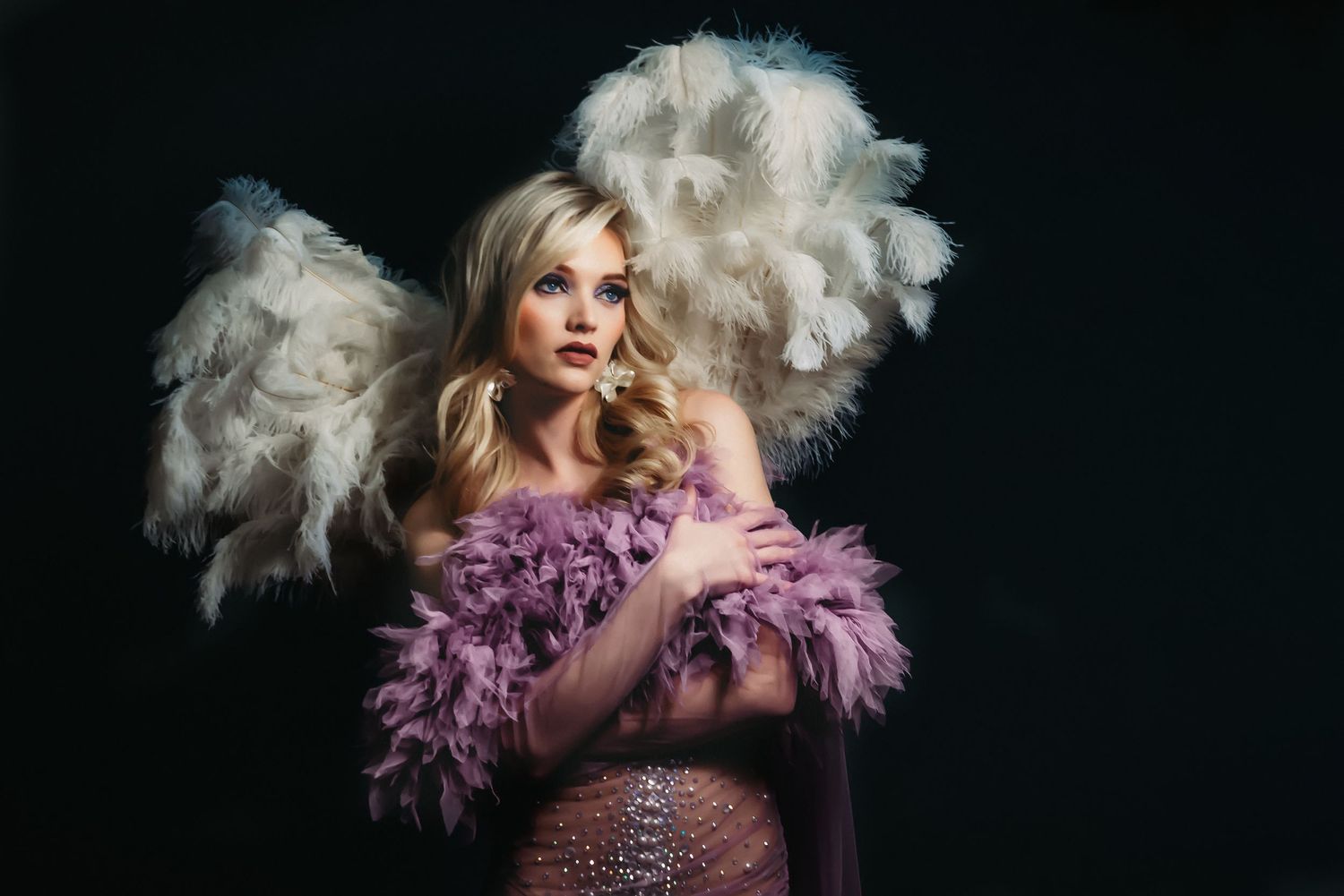 Glamorous portrait with white and purple feathers against dark background.