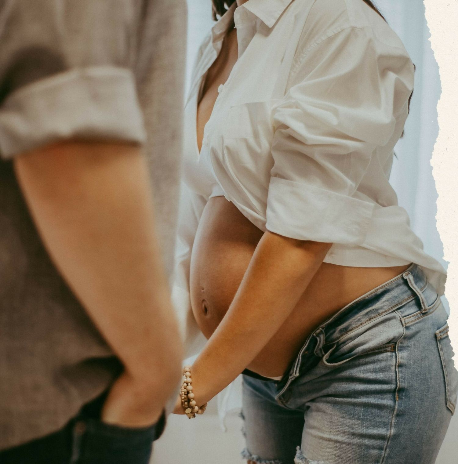 Maternity photo showing pregnant belly in casual white shirt and jeans.