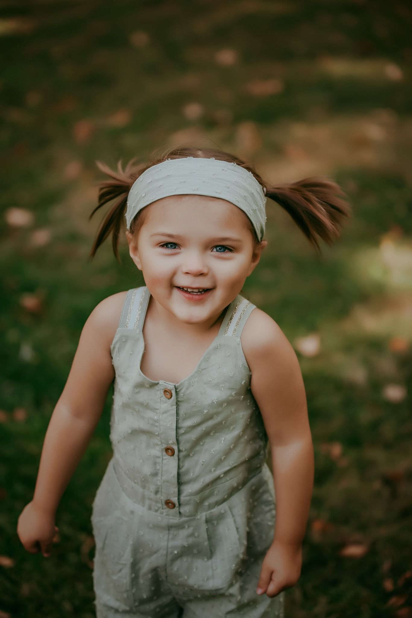 Young child in sage green romper playing outdoors in autumn.