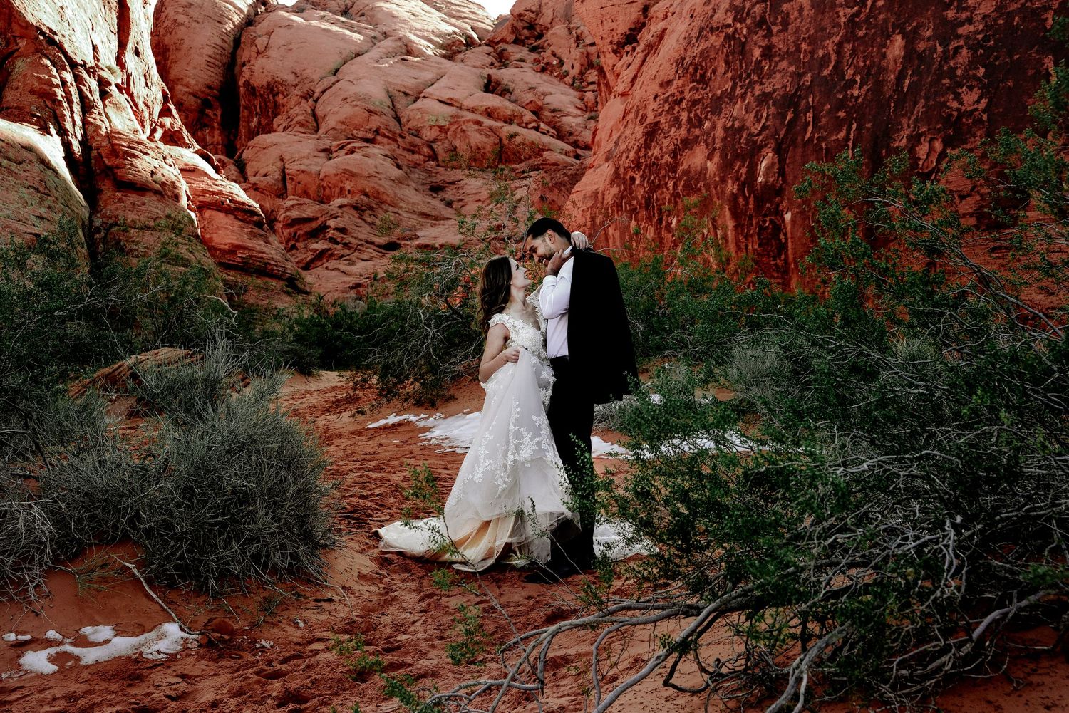Wedding couple poses among red rock formations in desert landscape.