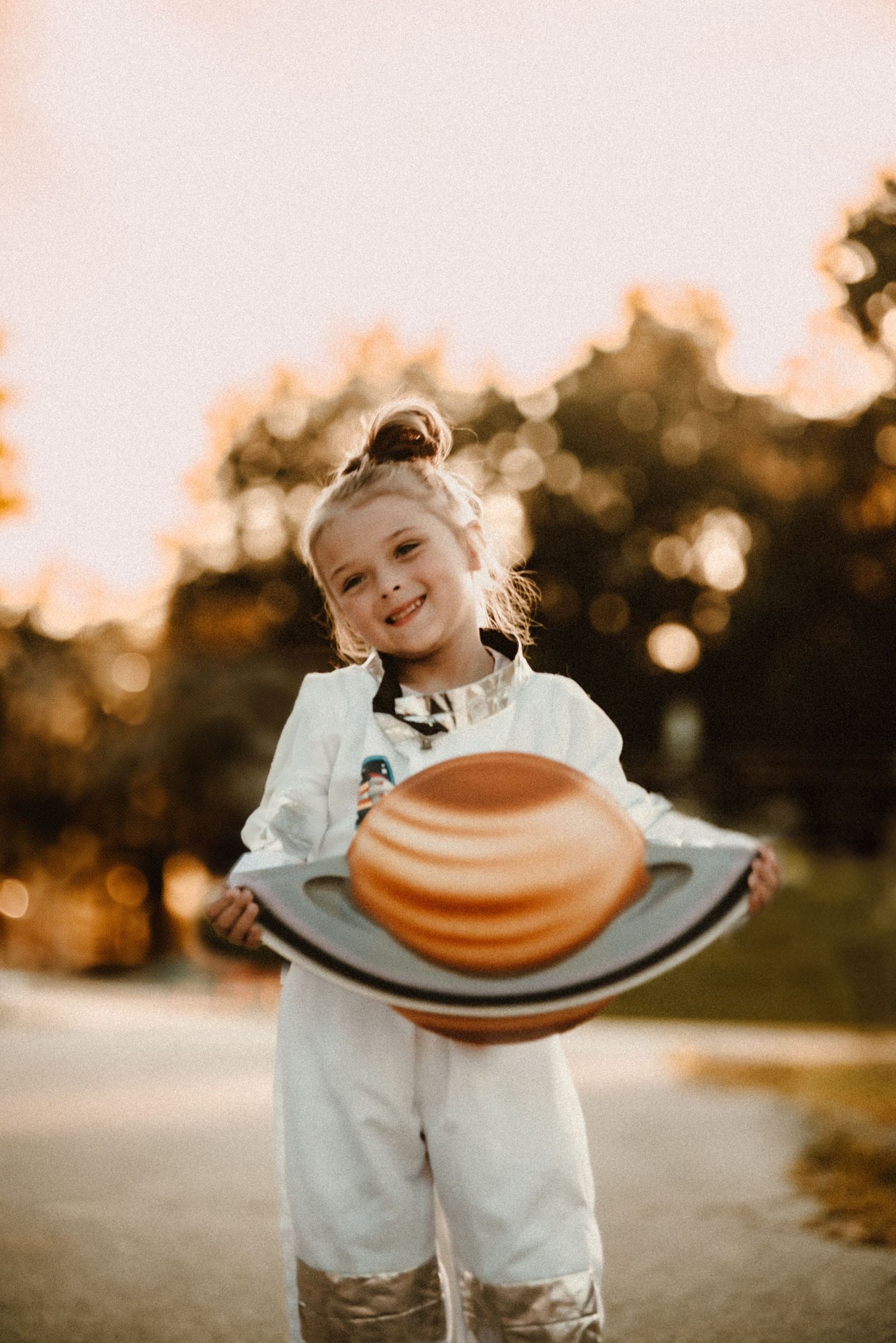 Child in space suit costume holds planet prop during golden hour photoshoot.