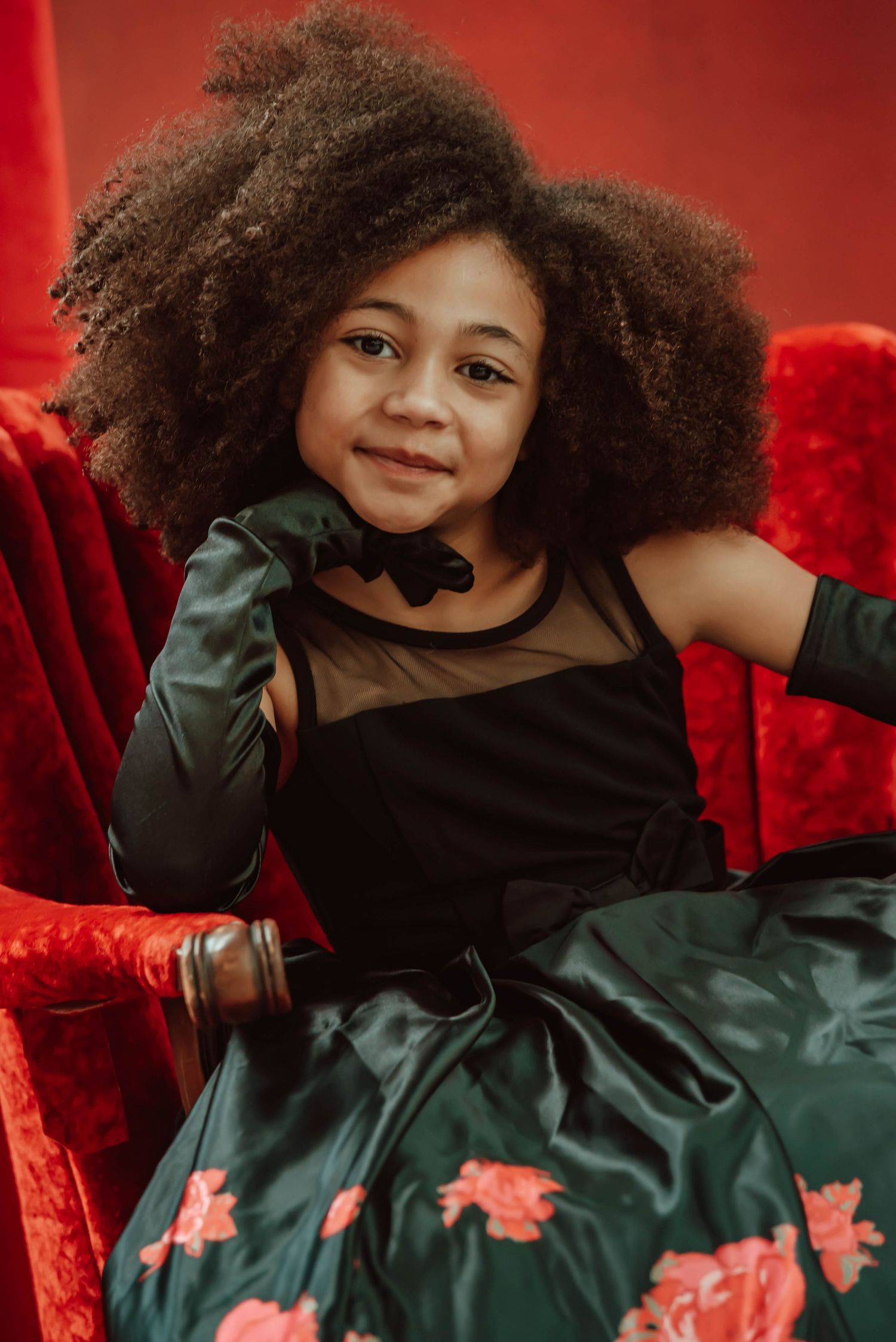 Portrait in emerald dress with floral details against red velvet chair.