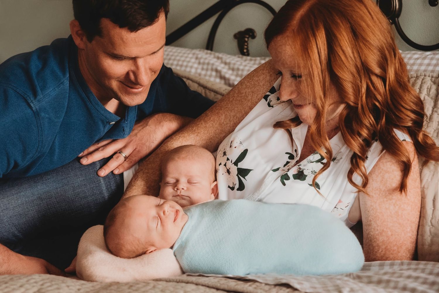 Intimate family moment with sleeping newborn on bed.