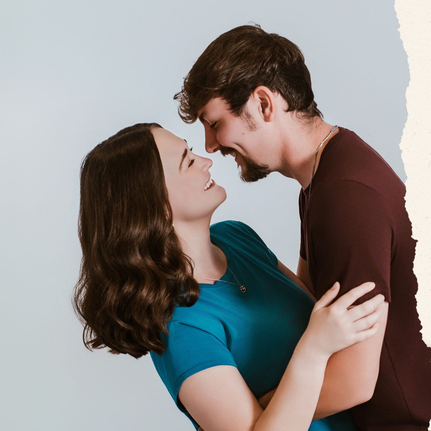 Romantic couple in blue and brown clothing embracing against light background.