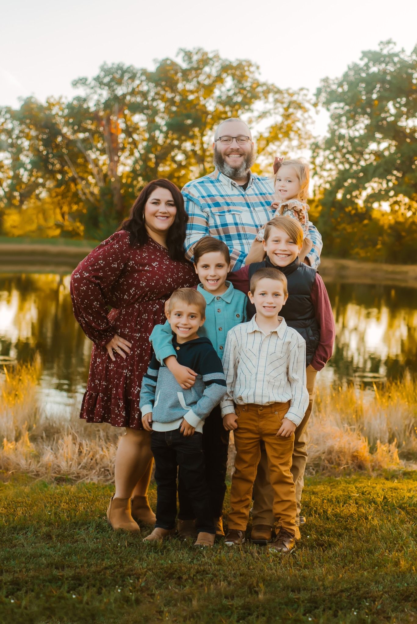 Family portrait session by a lake during golden hour with fall foliage in background.
