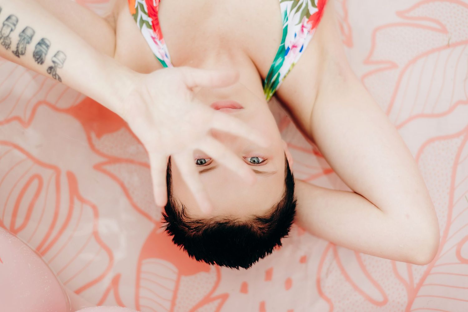 Overhead view of someone lying on a pink pool float with floral pattern design.