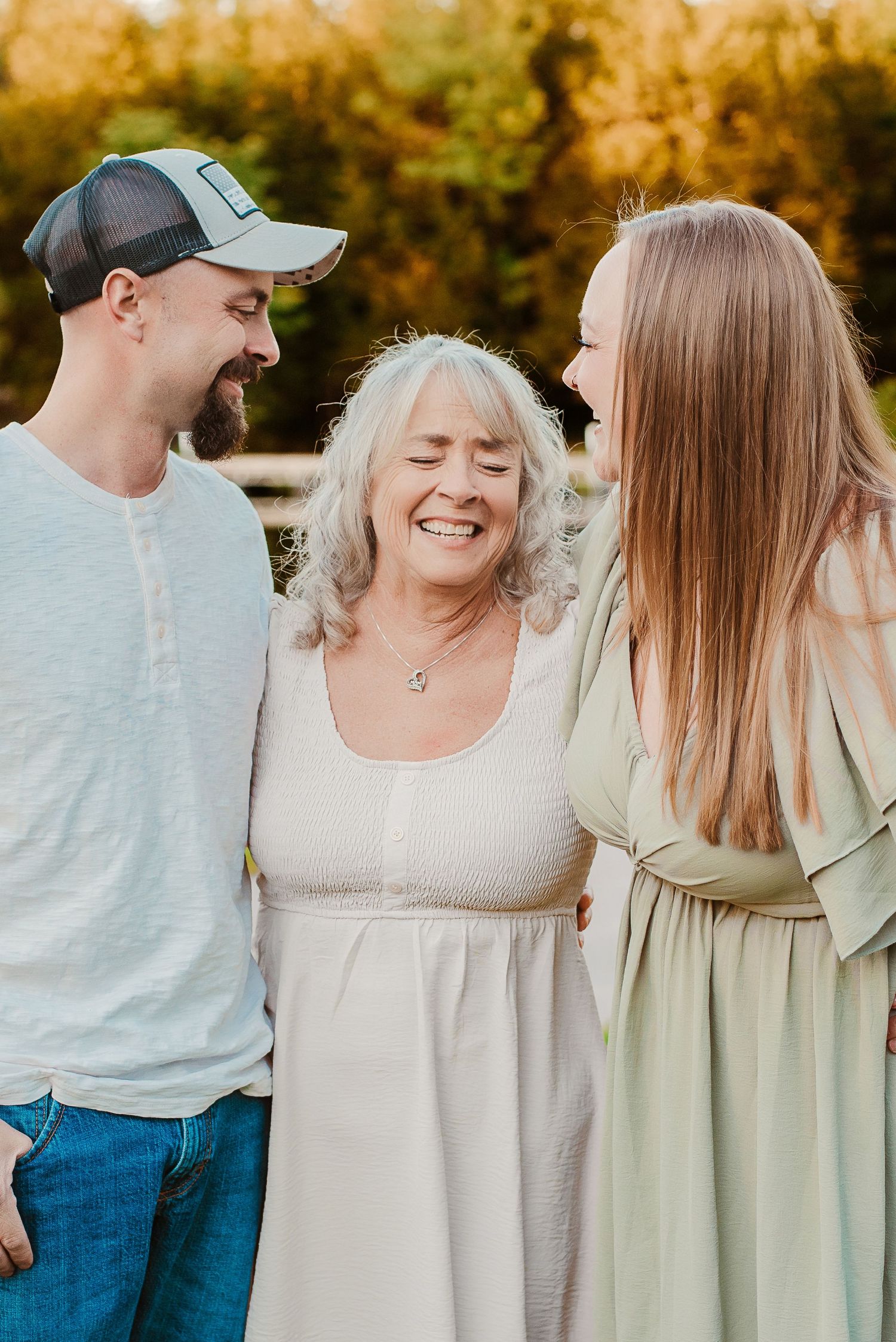 Three generations of family smiling together outdoors in warm golden light, wearing casual summer attire.