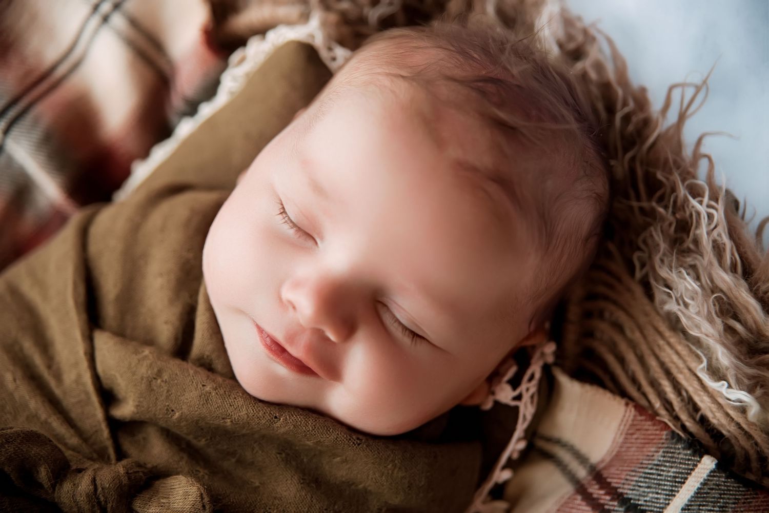 Sleeping baby wrapped in brown blanket during newborn photography session.