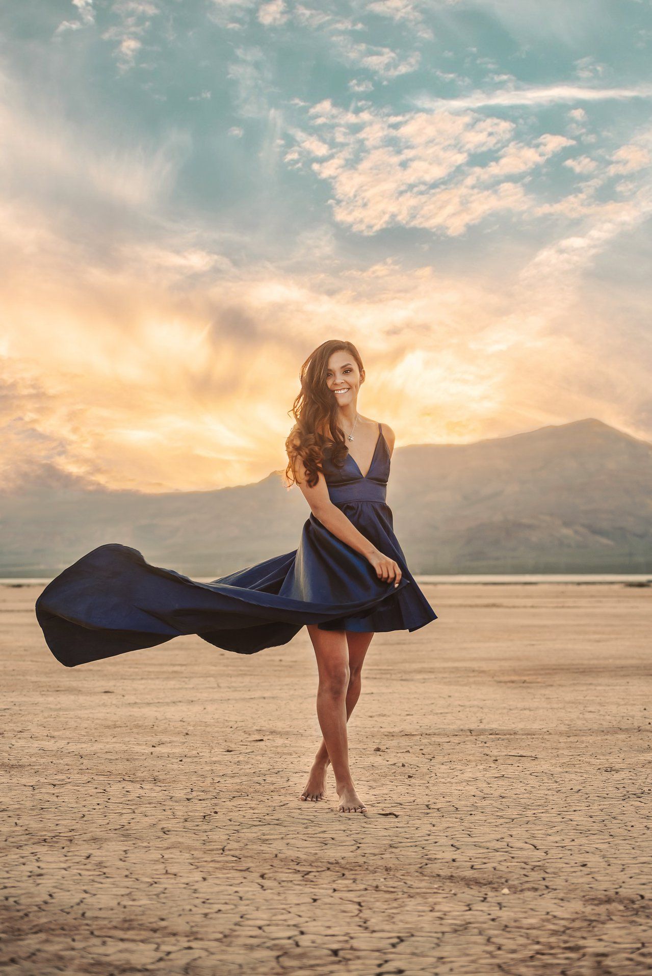 A flowing navy blue dress billows dramatically across a desert landscape at sunset.