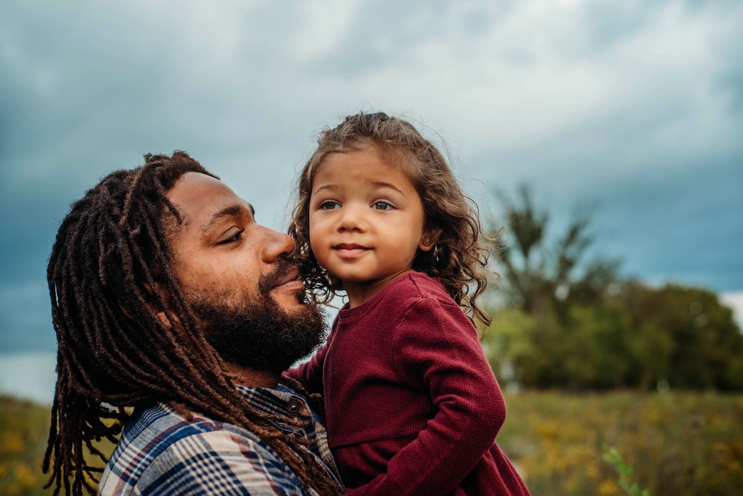 Candid outdoor portrait of parent and child sharing a joyful moment against cloudy sky.