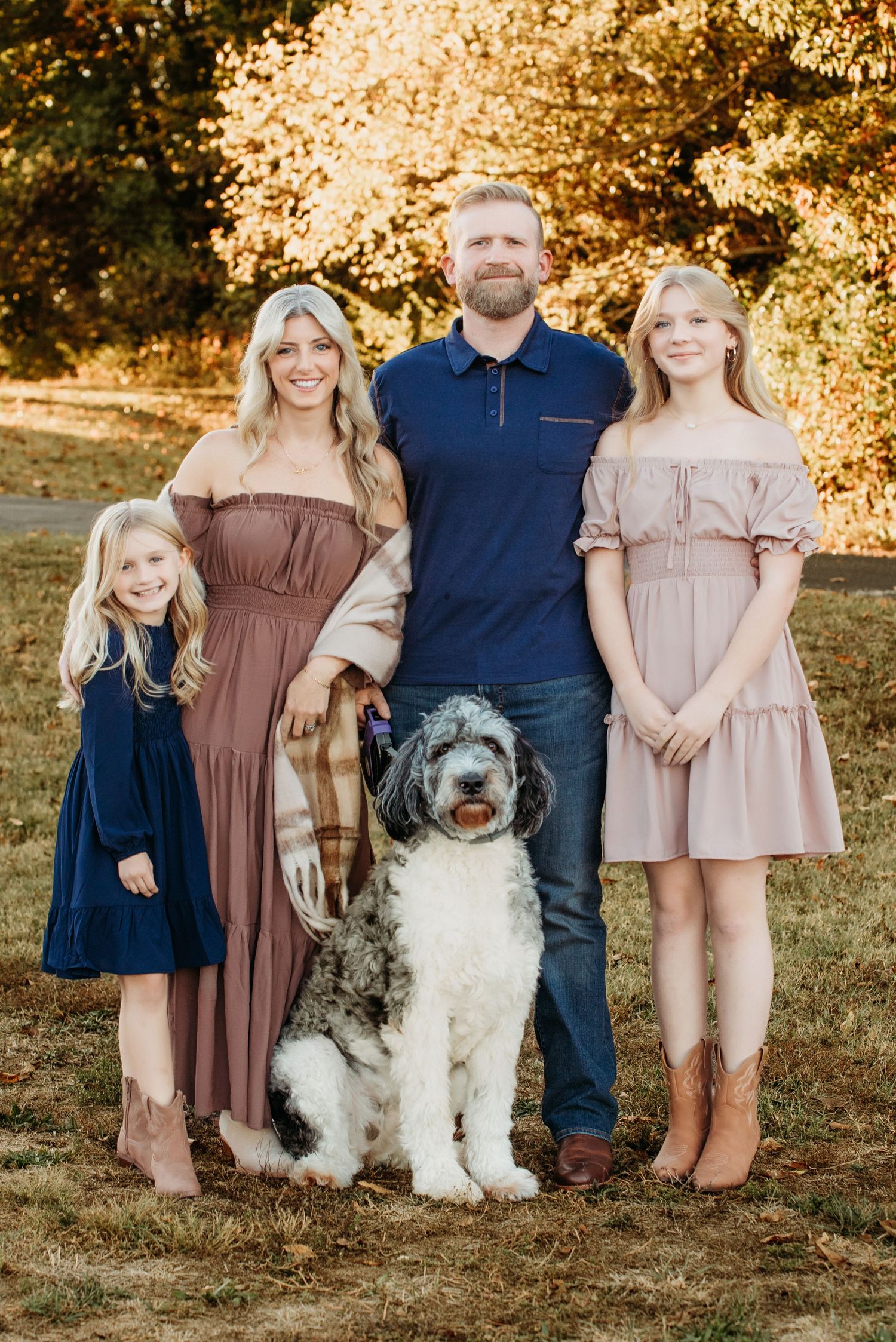 Family portrait with large doodle dog outdoors during golden hour with fall foliage backdrop.