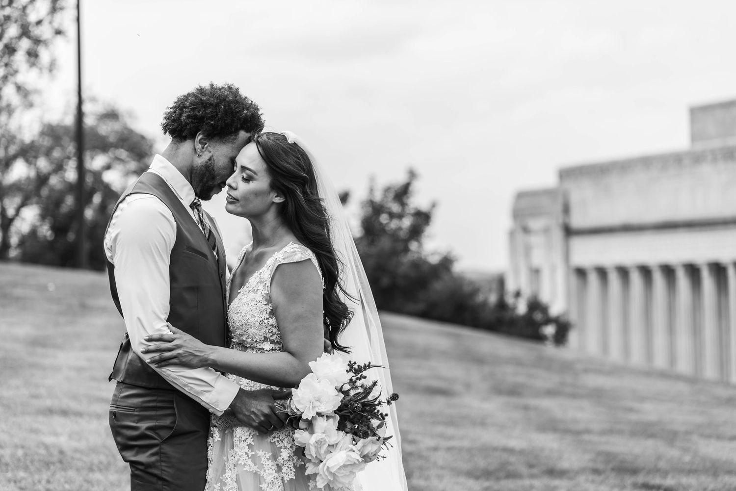 Romantic outdoor wedding photo session with a couple embracing on a grassy hillside.