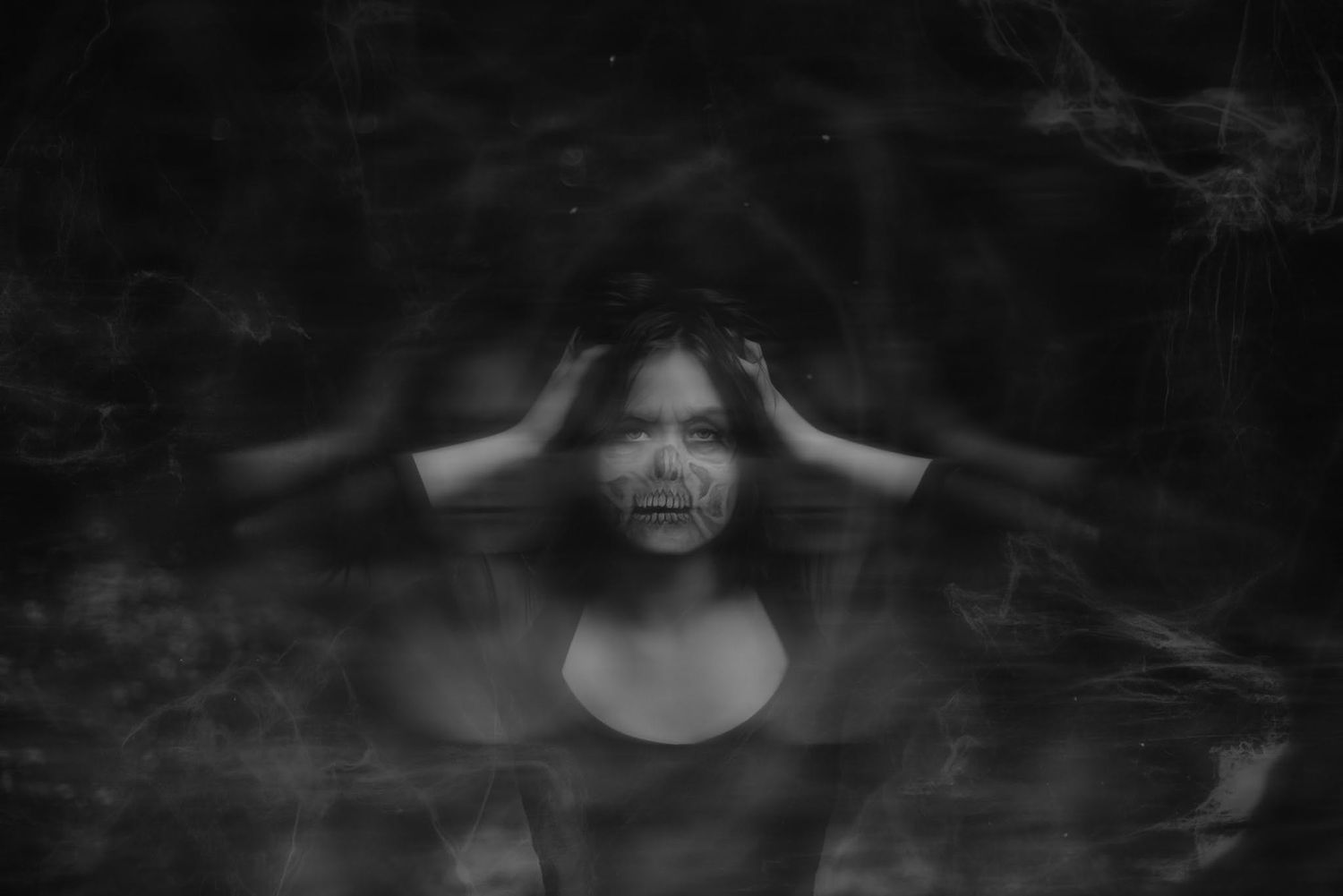 Black and white double exposure portrait of distressed woman holding her head against dark moody background.