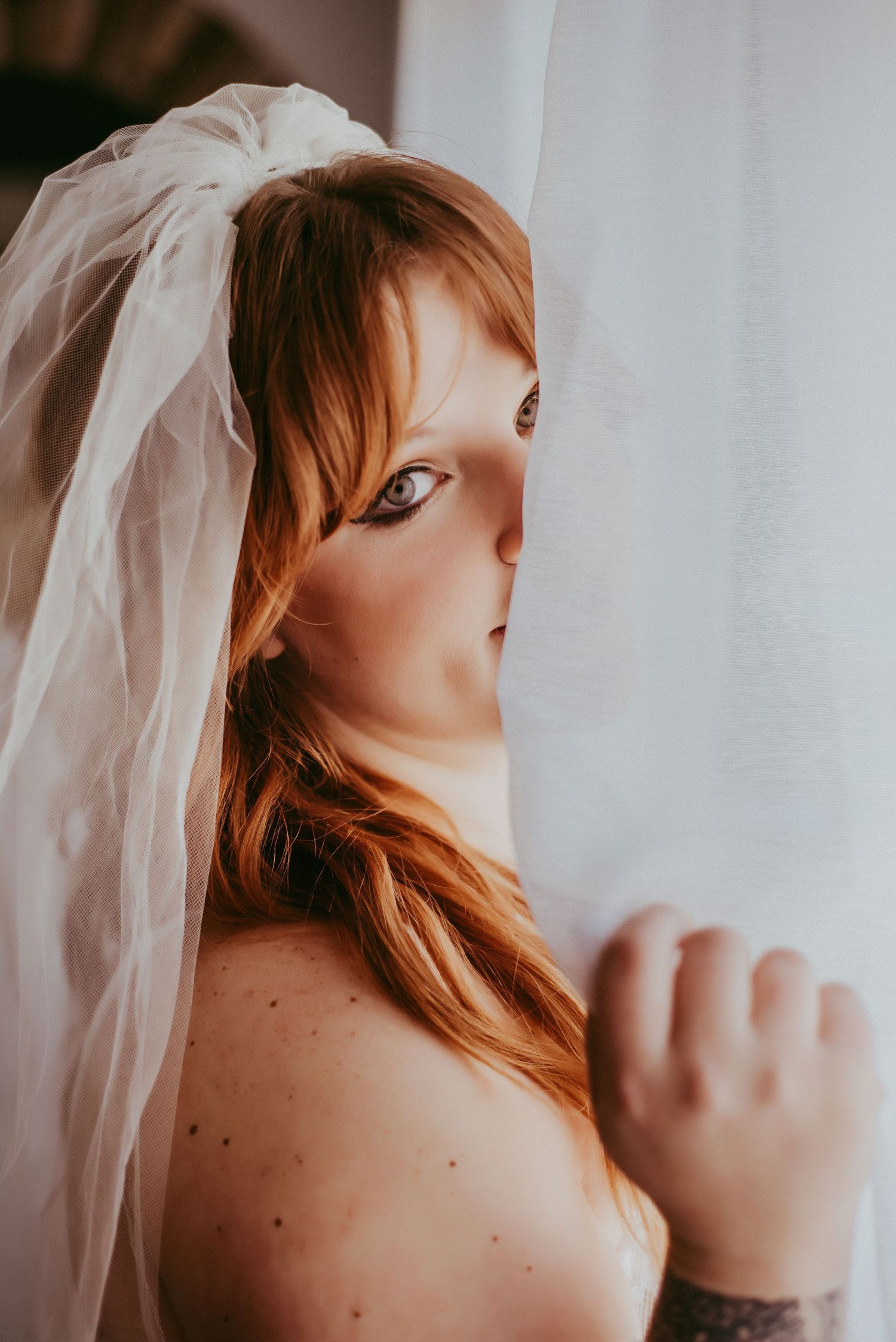 Artistic bridal portrait with flowing veil against white background.