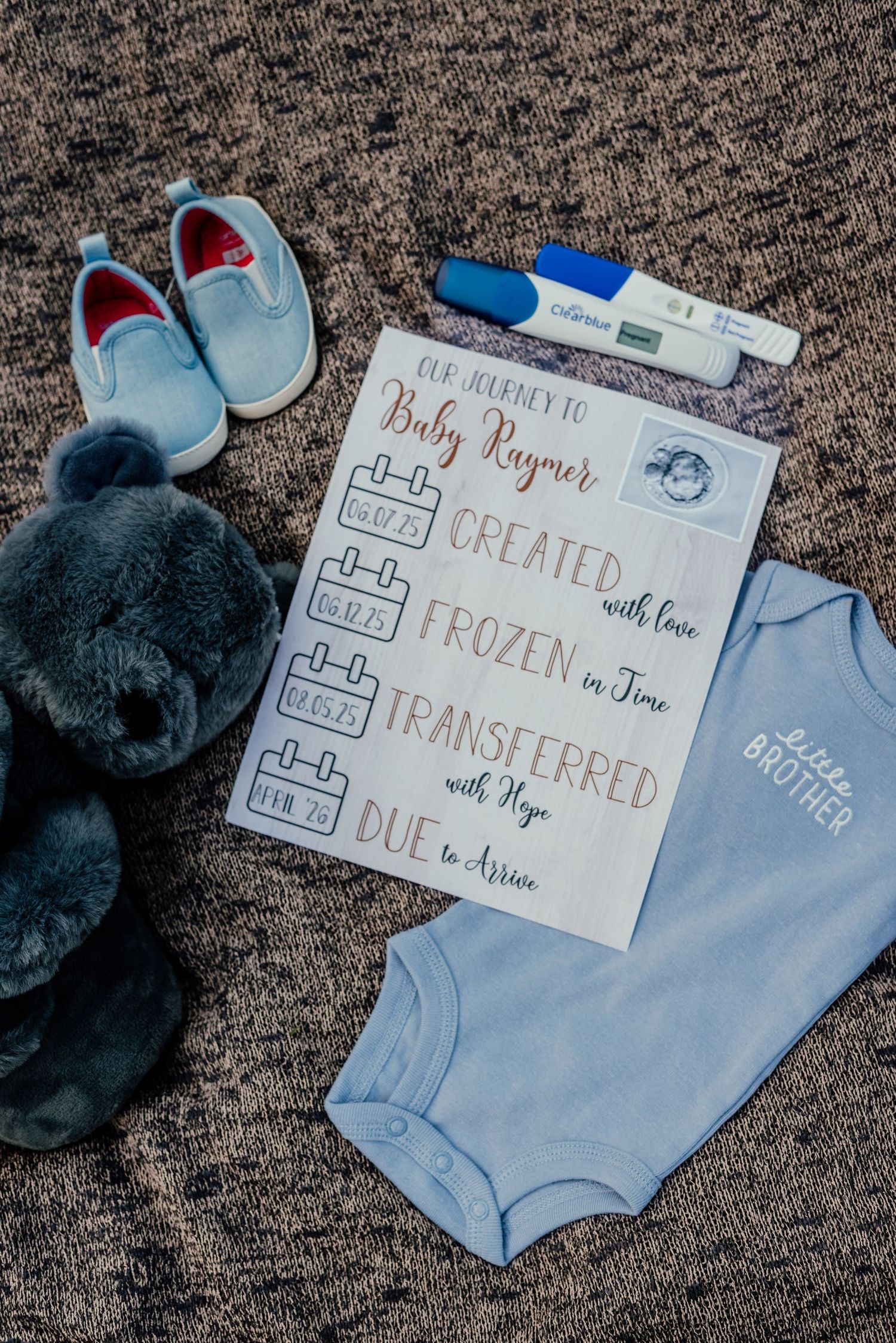 Baby announcement display with blue onesie and handwritten card on carpet.