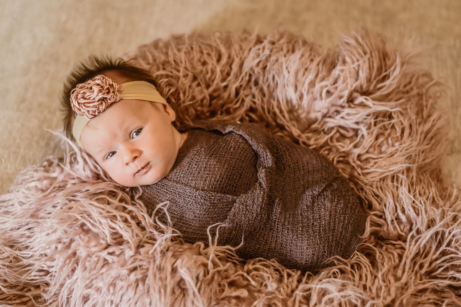 Newborn baby lying on soft fluffy beige blanket during professional photo session.