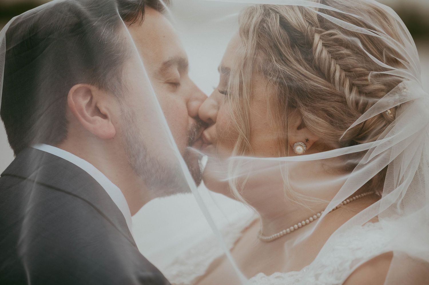 Intimate wedding kiss captured in soft, dreamy lighting with bride's veil flowing.