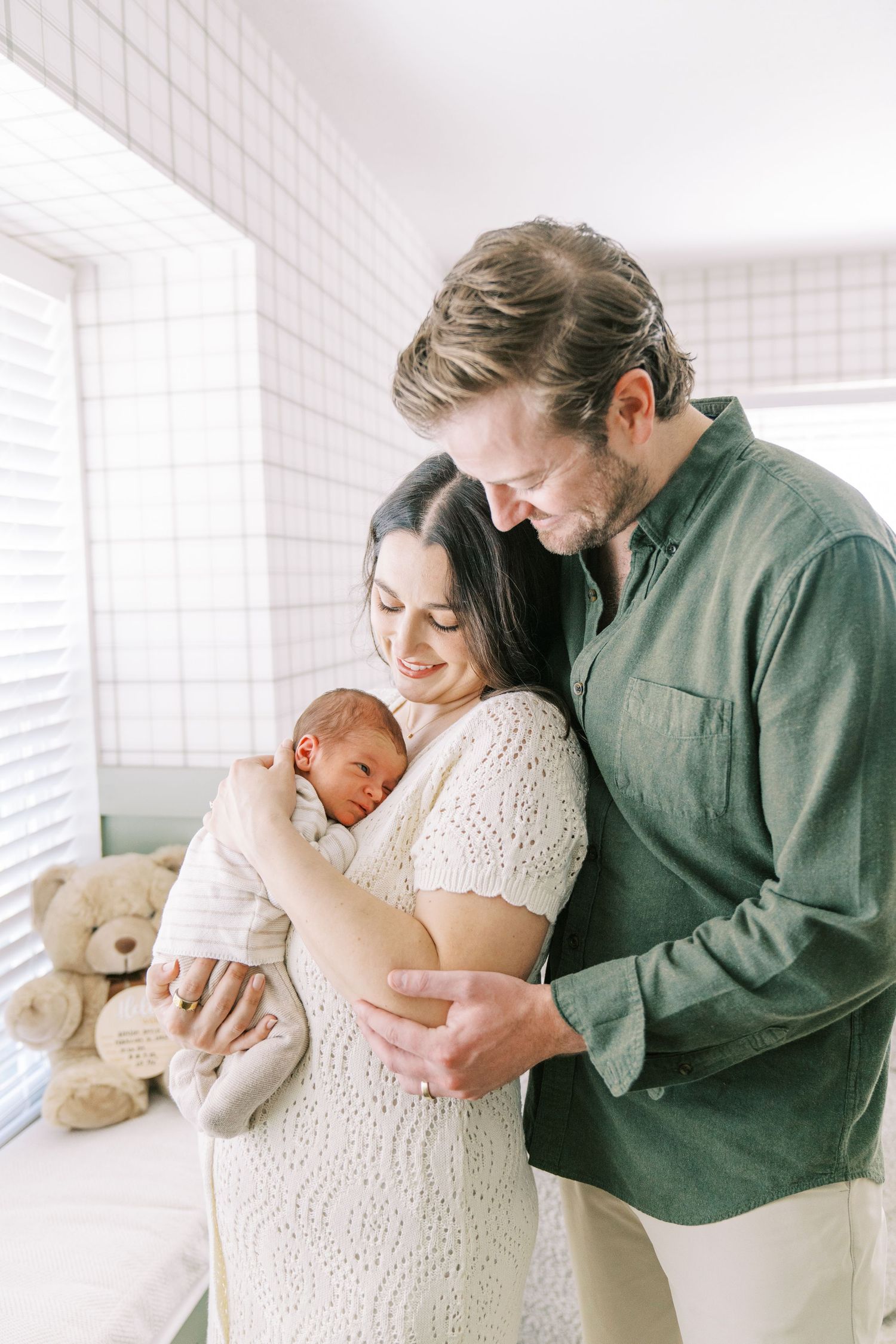 A tender family moment captured in a bright white room with a teddy bear as they embrace lovingly.