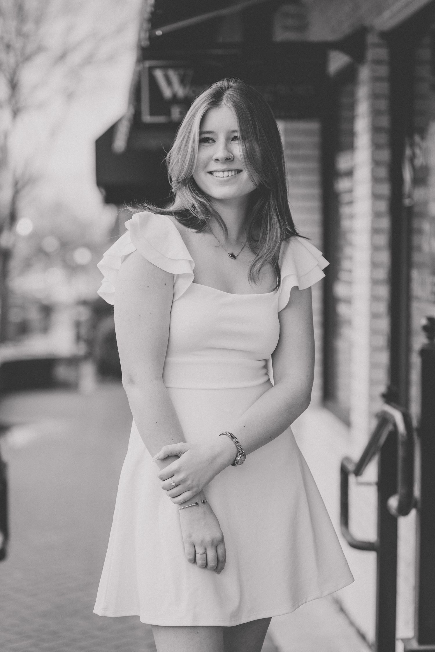 A person wearing a white ruffled dress stands outside a brick building in a black and white photograph.
