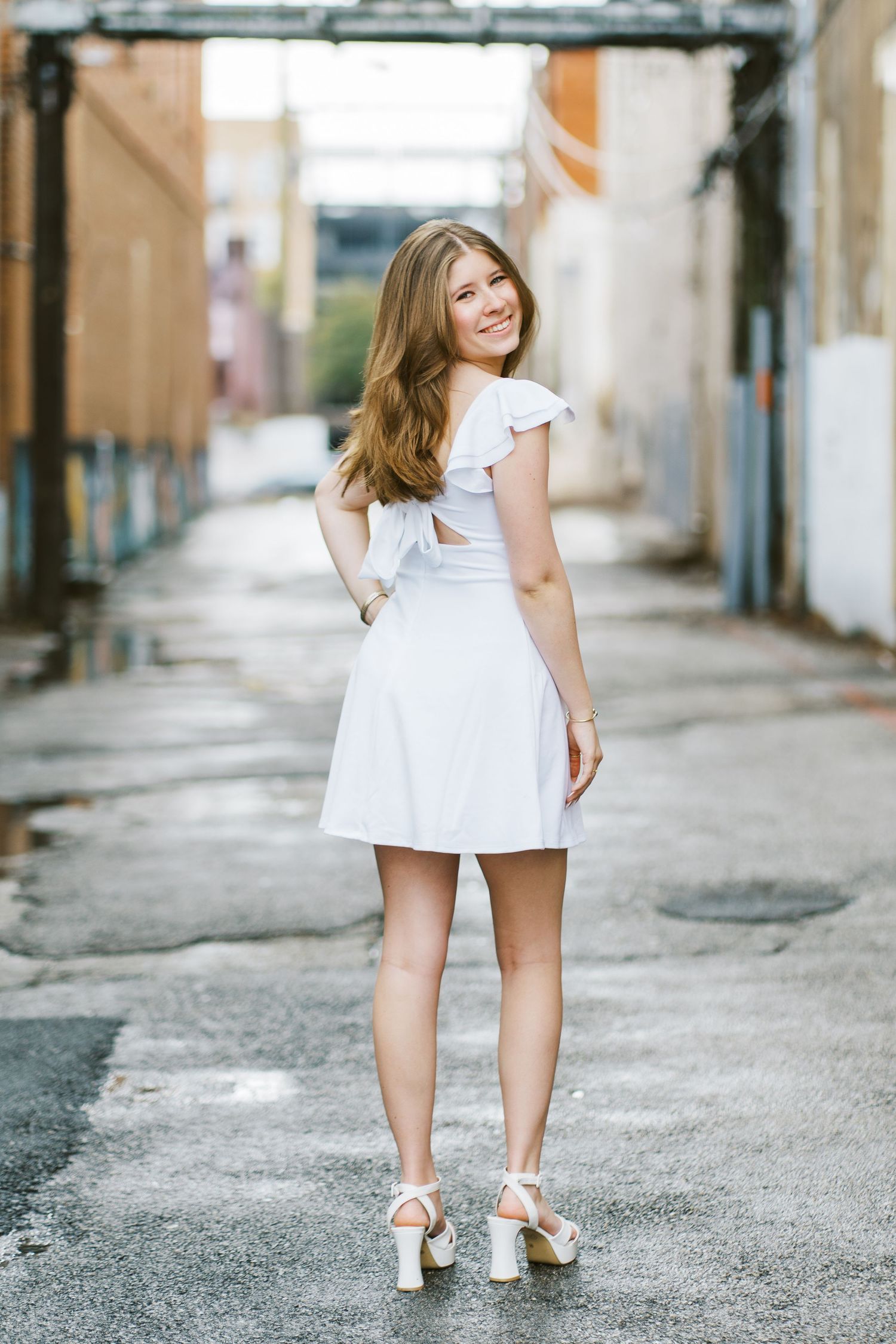 A person in a white dress and heels poses in various angles on a gritty urban street.