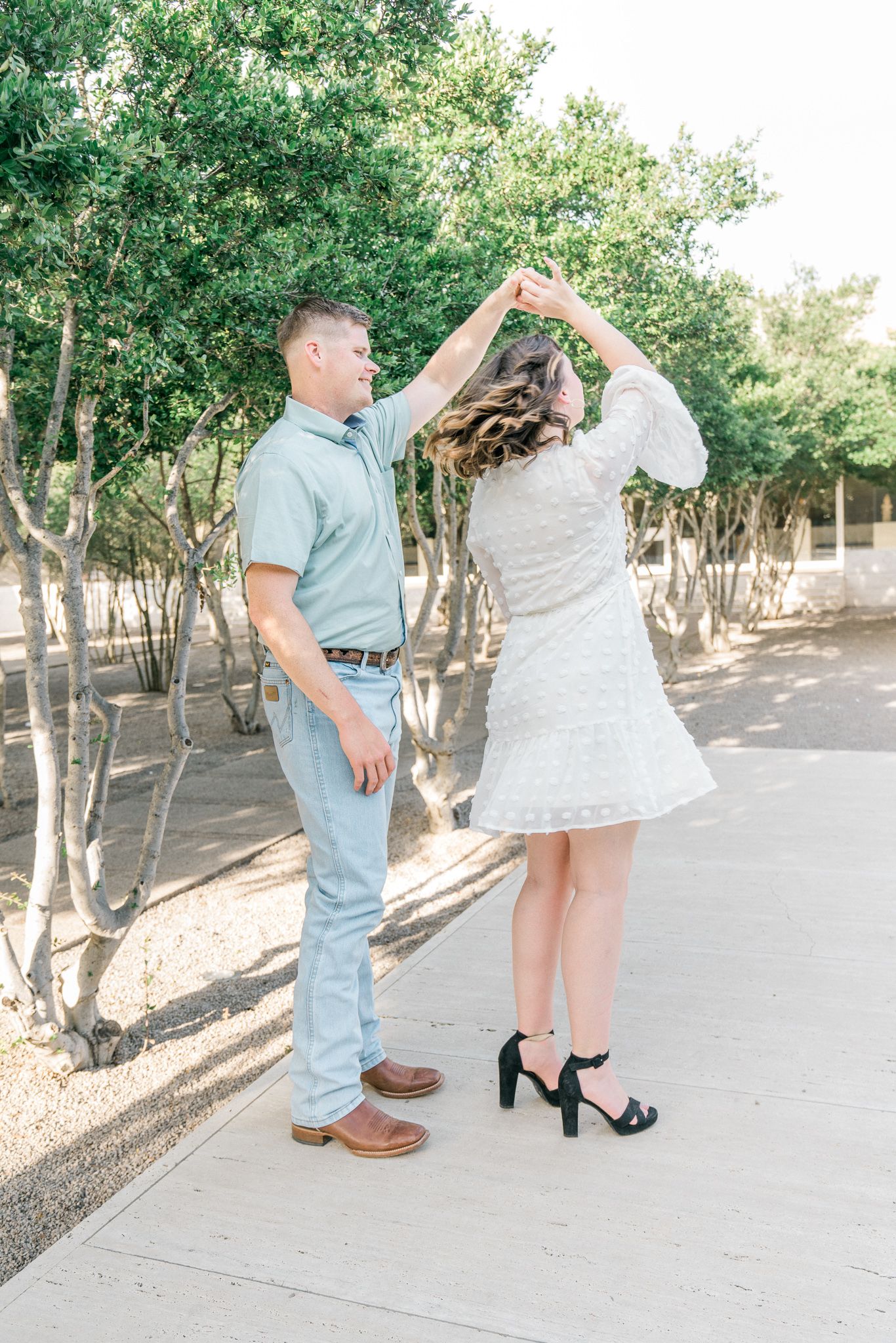 Couple in casual summer outfits dancing and twirling in outdoor garden setting.
